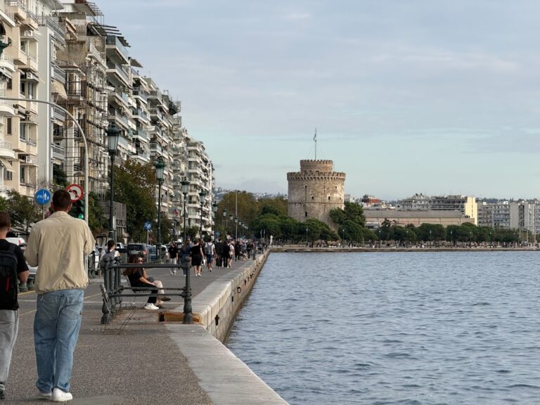 People walking along the waterfront with white tower building.