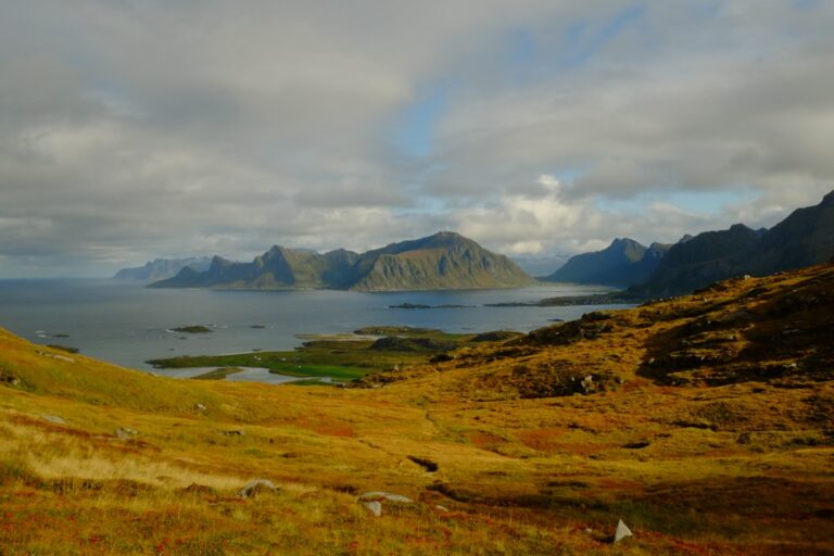 Mountainous coastline with calm sea under cloudy sky.